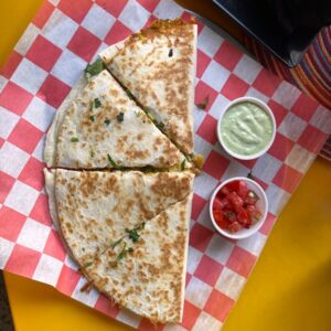 A quesadilla cut in half on a red and white checkered paper