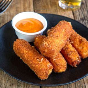 A black plate topped with fried food next to a cup of dipping sauce
